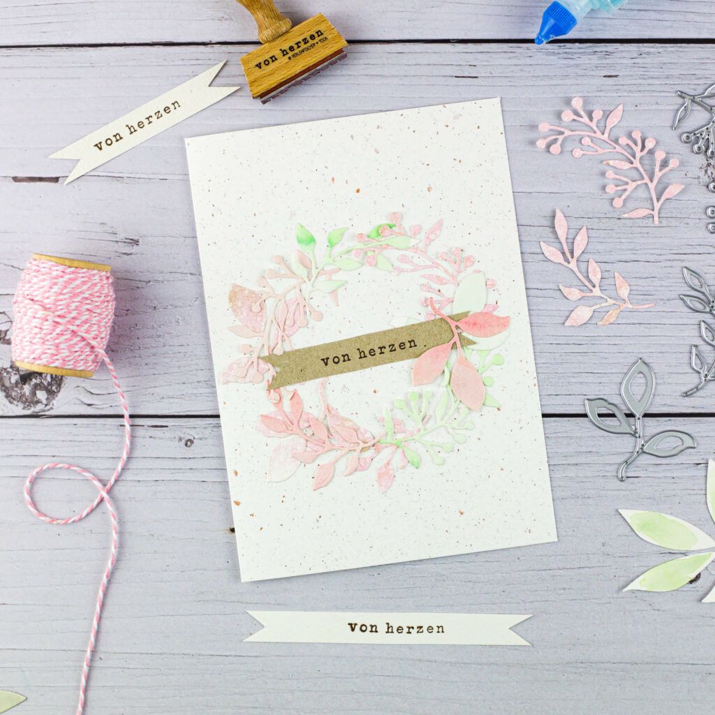 Grusskarte mit Kranz aus Papierblättern und Zweigen